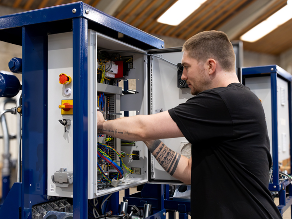 A technician working on an open electrical cabinet, inspecting and managing internal wiring and components in a workshop setting.