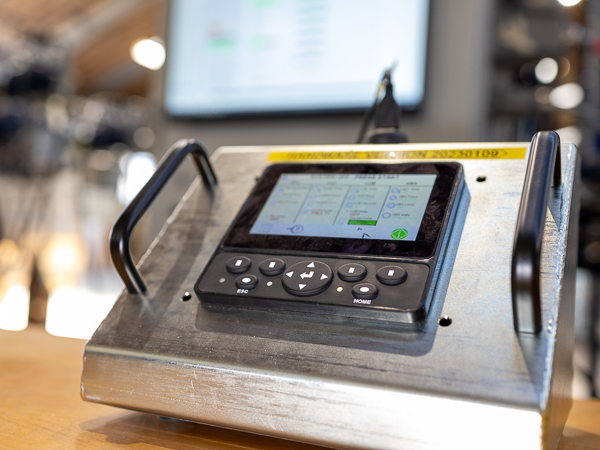 A control device with a screen and buttons on a sturdy metal stand, used for operating machinery or testing systems.