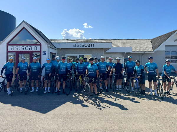 21 riders from Lemvig Cycling Club in blue jerseys standing with their bikes in front of the AS SCAN building after a 155 km ride.